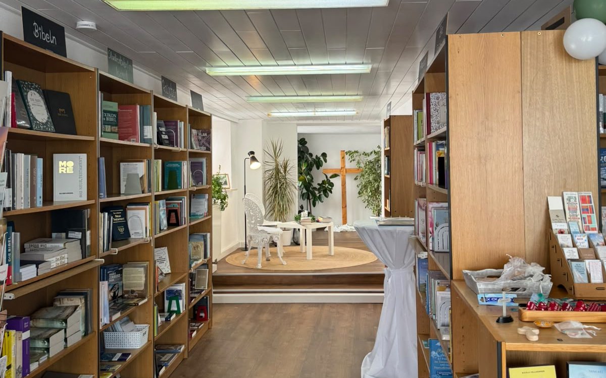 Blick durch den Laden: Bibel-Regale, dahinter das Holzkreuz und die Leseecke